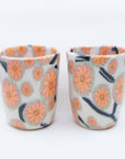 Pair of handmade cups patterned with pink cherry blossom flowers on black branches.