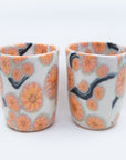 Pair of handmade cups patterned with pink cherry blossom flowers on black branches.