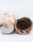 Pair of handmade cups patterned with pink cherry blossom flowers on black branches. Bottom and inside view.