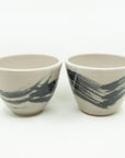 Pair of grey porcelain cups painted with one large black brushstroke and splattered with white all around.