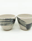 Pair of grey porcelain cups painted with one large black brushstroke and splattered with white all around.