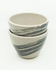 Pair of grey porcelain cups painted with one large black brushstroke and splattered with white all around. Stacked together.