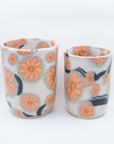 Pair of handmade cups patterned with pink cherry blossom flowers on black branches.