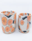 Pair of handmade cups patterned with pink cherry blossom flowers on black branches. Bottom and inside view.