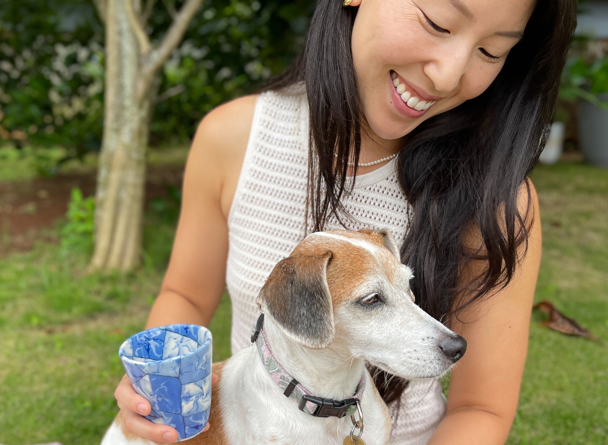 Woman holding handmade cup with dog sitting on her lap.